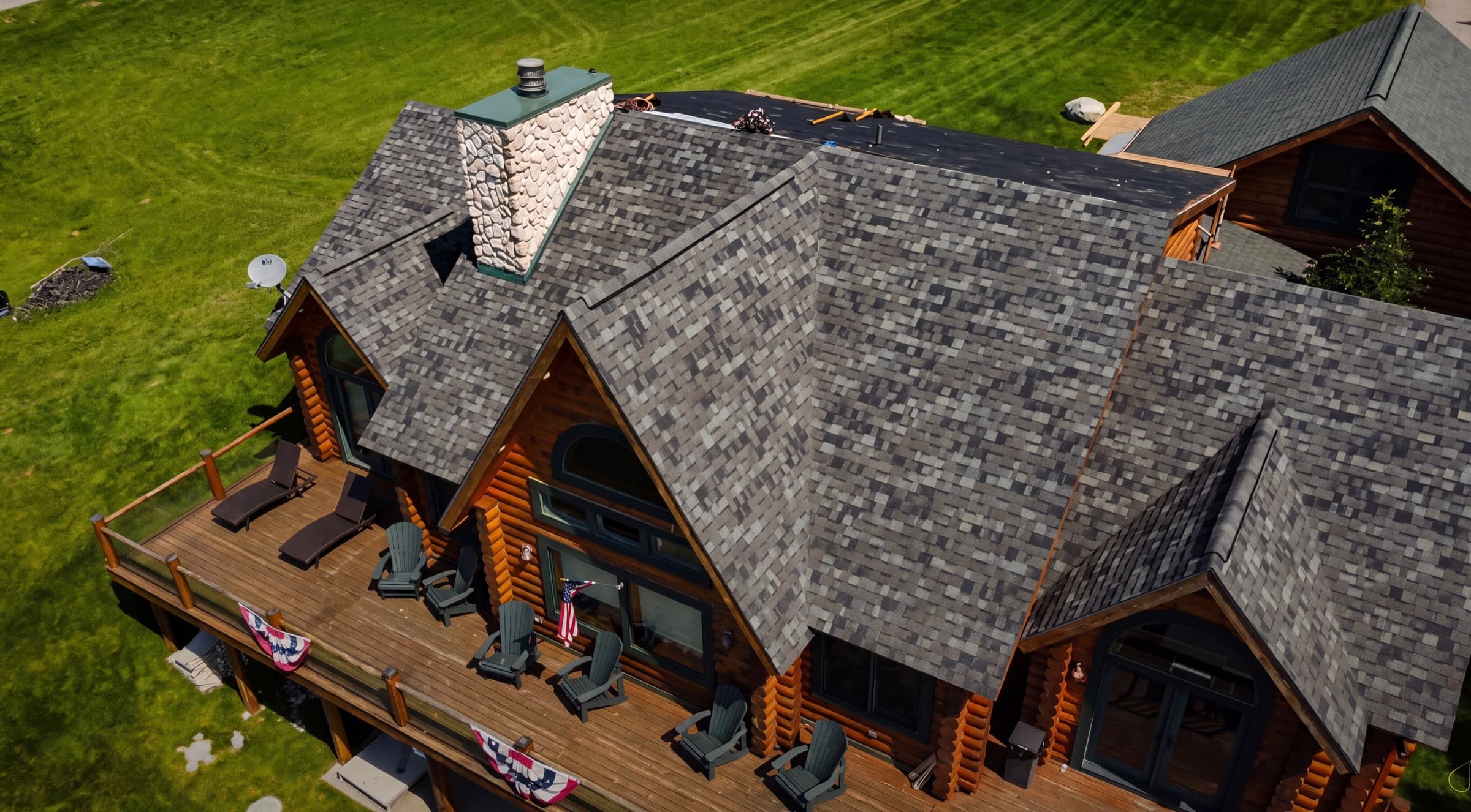 Aerial view of a BR Construction project — multi-pitch architectural shingle roof on a Northern Michigan timber home with a wraparound deck